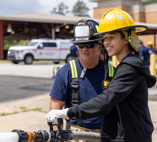 An intern next to a firefighter using the water hose