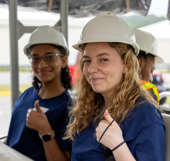 Two happy interns seating on a bus wearing a helmet