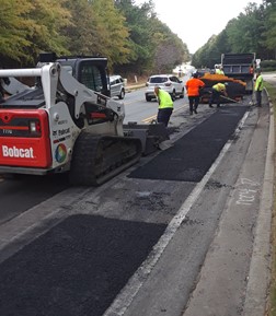 construction workers laying new asphalt over sections of roadway